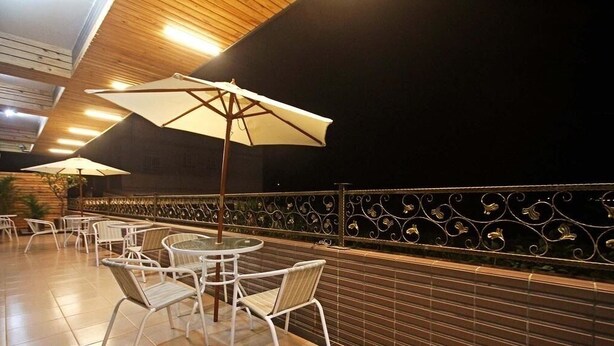 Un área de patio al aire libre con mesas y sillas redondas, sombrillas grandes y una barandilla metálica decorativa.