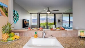 A kitchen with a large window, a ceiling fan, and a sink.