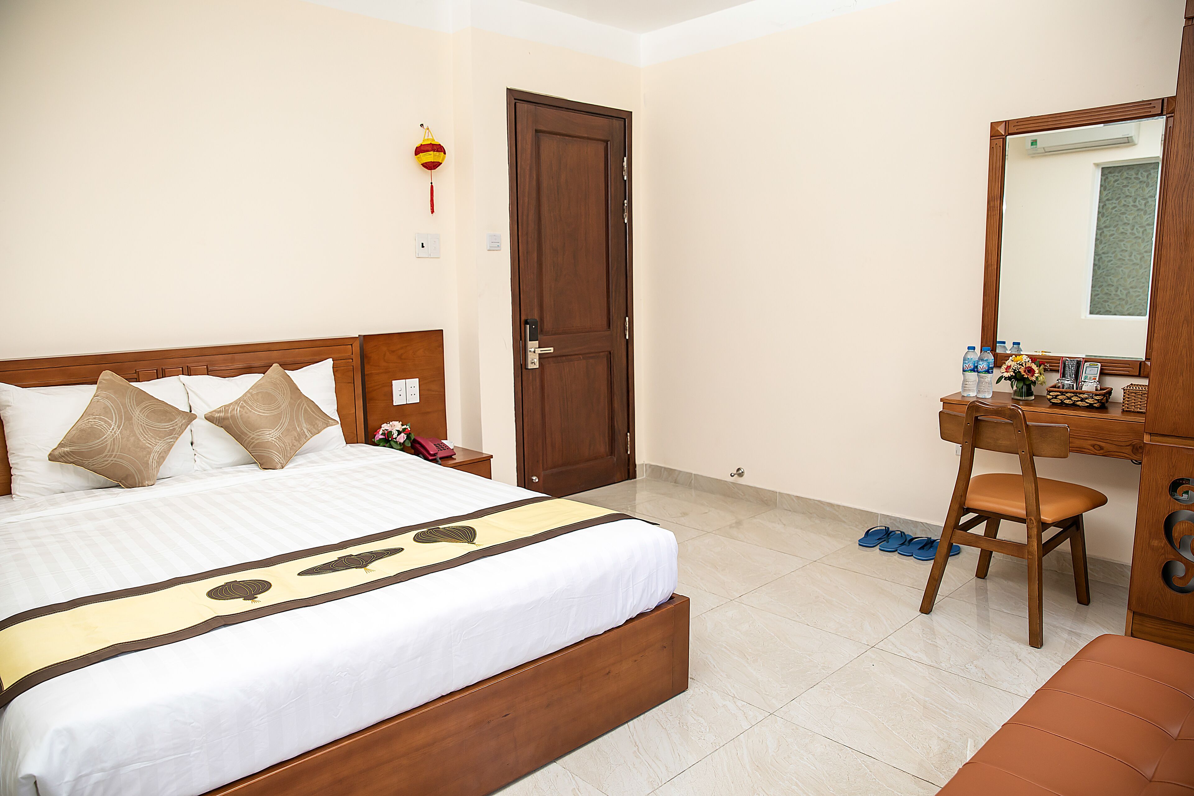 A neatly arranged hotel room with a large bed, a wooden desk, a chair, and a mirror.