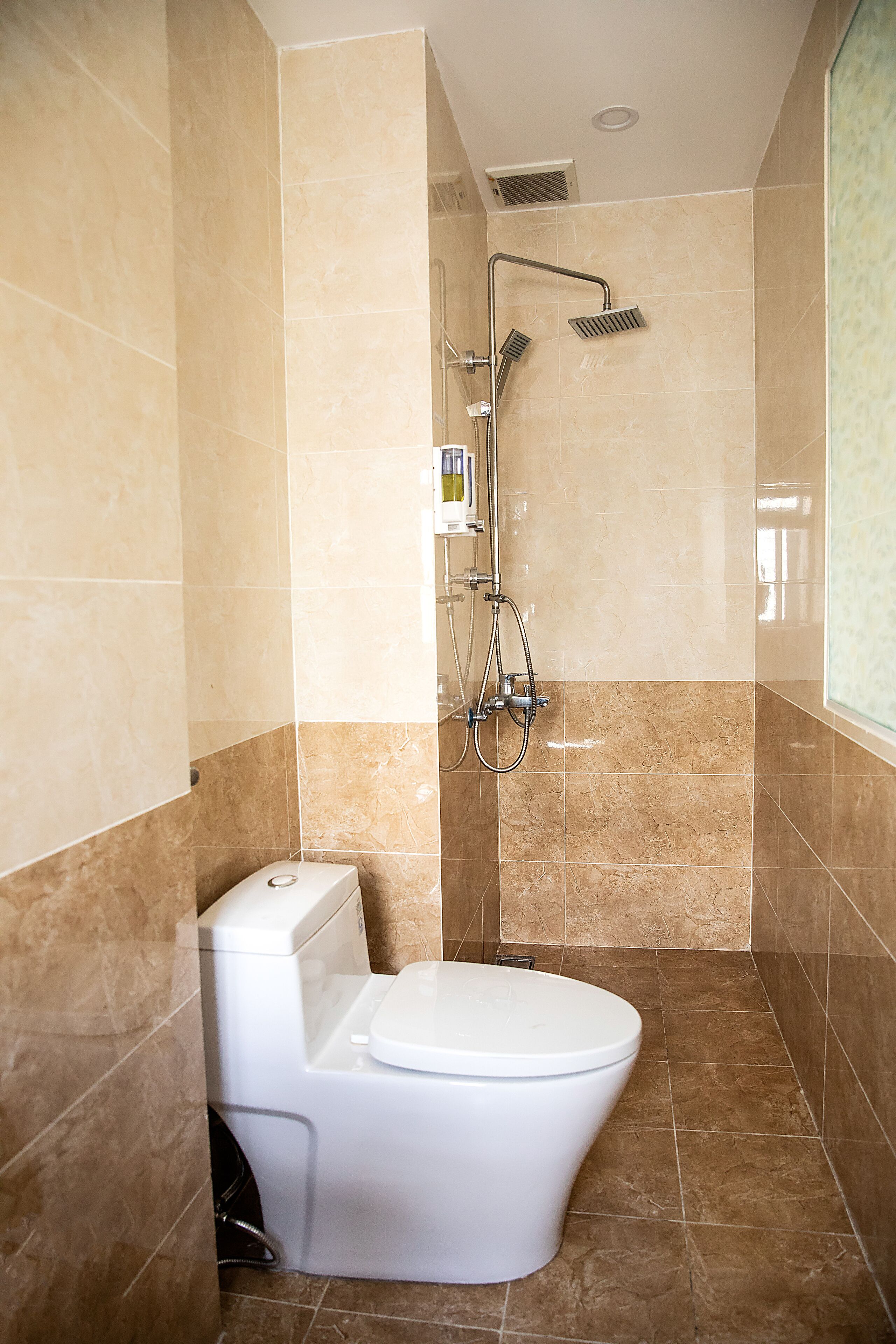 A bathroom with a toilet, a shower, and a tiled floor.