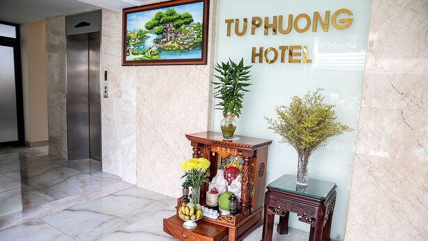 A reception area with a marble floor, a wooden cabinet with decorative items, a small table with a vase, and a painting above the elevator. - Tu Phuong Hotel (Ho Chi Minh City)