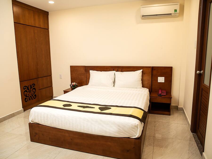 A neatly made bed with a wooden headboard, a bedside table with a phone, and an air conditioning unit on the wall.