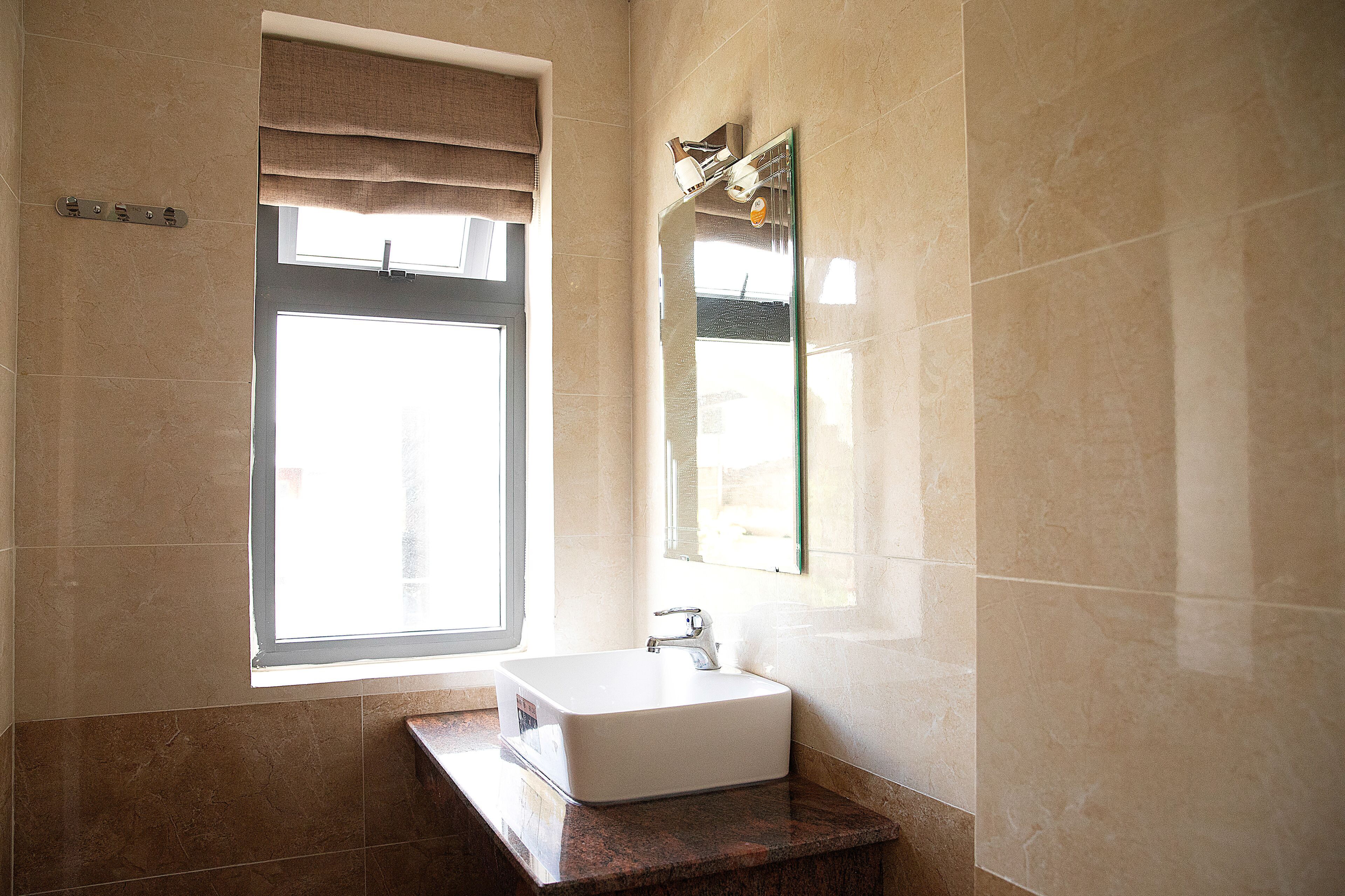 Un baño con un amplio ventanal, un lavamanos blanco y un espejo.