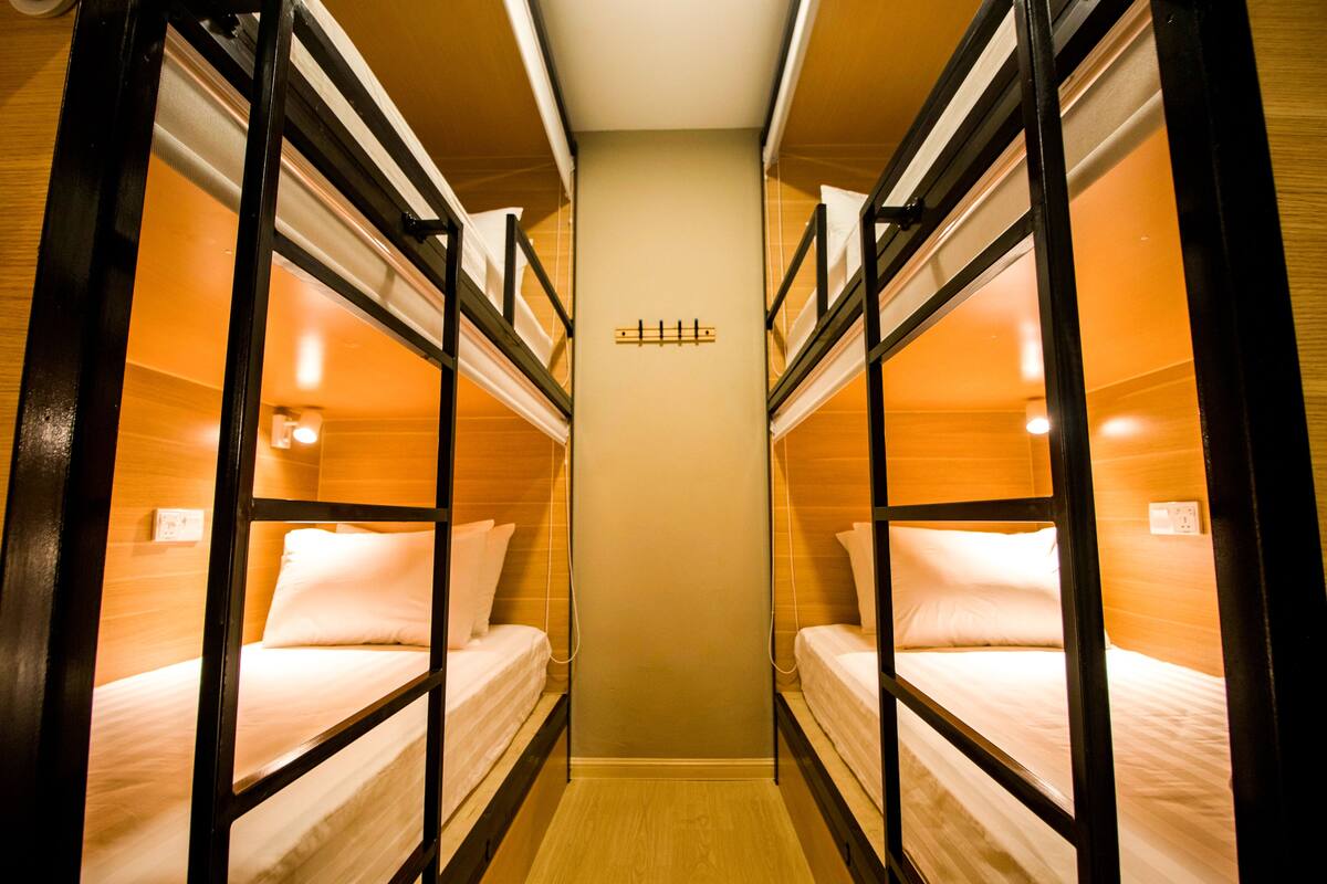 A narrow corridor with bunk beds on either side, a central light fixture, and a wall-mounted switch.