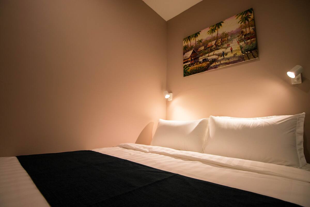 A hotel room with a bed, a painting on the wall, and two wall-mounted lights.