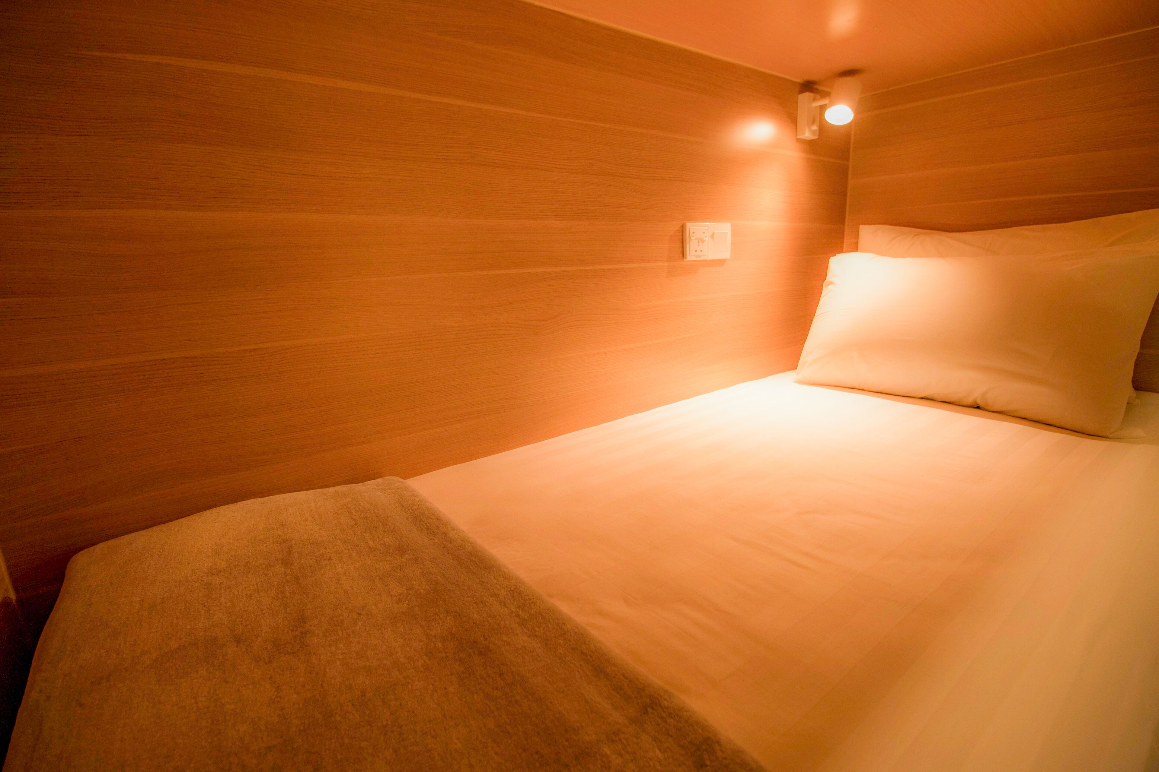 Una cama bien hecha con edredón blanco y almohadas, cabecera de madera y una lámpara de pared.