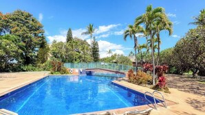 A rectangular swimming pool with a blue water surface, surrounded by a brick deck and metal poolside chairs. - Spacious Koa Resort Condo, Across Street From Beac (Kihei)