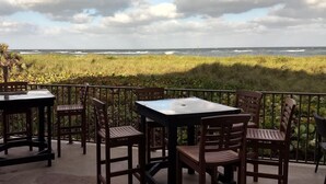 Un patio al aire libre con mesas y sillas, con vistas a un área verde y el océano.