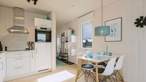 A modern kitchen with white cabinetry, a stainless steel range hood, and a dining area with a white table and chairs. - Cozy home in OstseeResort Olpenitz with sauna (OstseeResort Olpenitz)