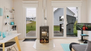 A modern living room with a fireplace, a television, and a view of a residential area. - Cozy home in OstseeResort Olpenitz with sauna (OstseeResort Olpenitz)