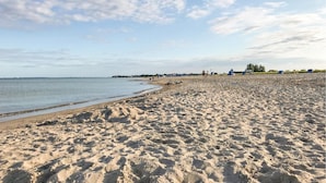 A wide sandy beach with gentle waves, a clear sky, and a distant shoreline with buildings and greenery. - Cozy home in OstseeResort Olpenitz with sauna (OstseeResort Olpenitz)