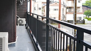 A balcony with a black railing, a white air conditioning unit, and a brown wall. - Station Business Hotel Tenshukaku Hitoyoshi (Hitoyoshi)