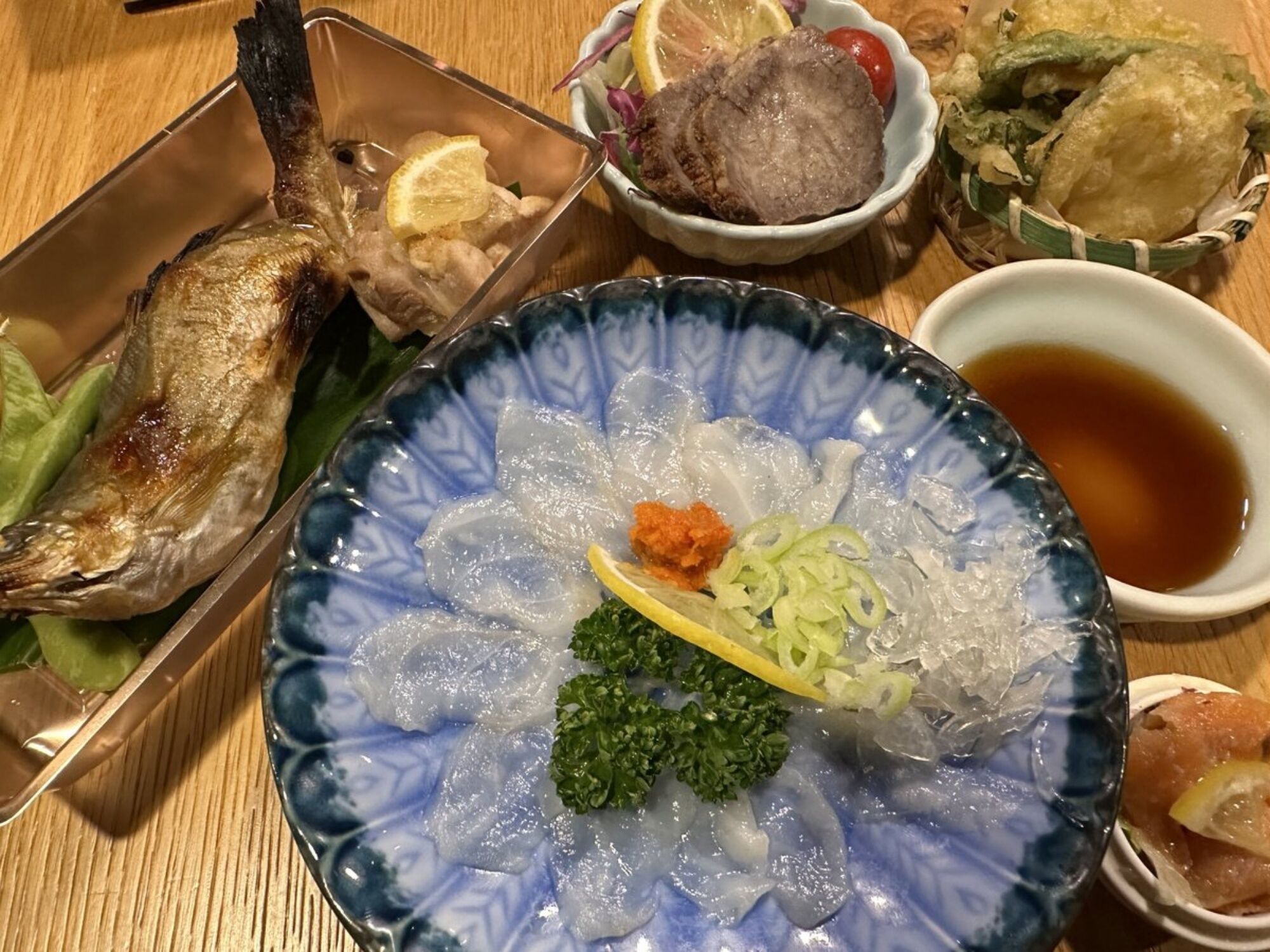 Variedad de platos que incluyen un bol de sashimi, un bol de sopa y un plato de pescado a la parrilla.