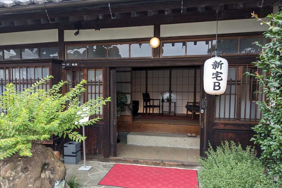 A traditional Japanese building with a wooden exterior, a red mat at the entrance, and a sign with Japanese characters.