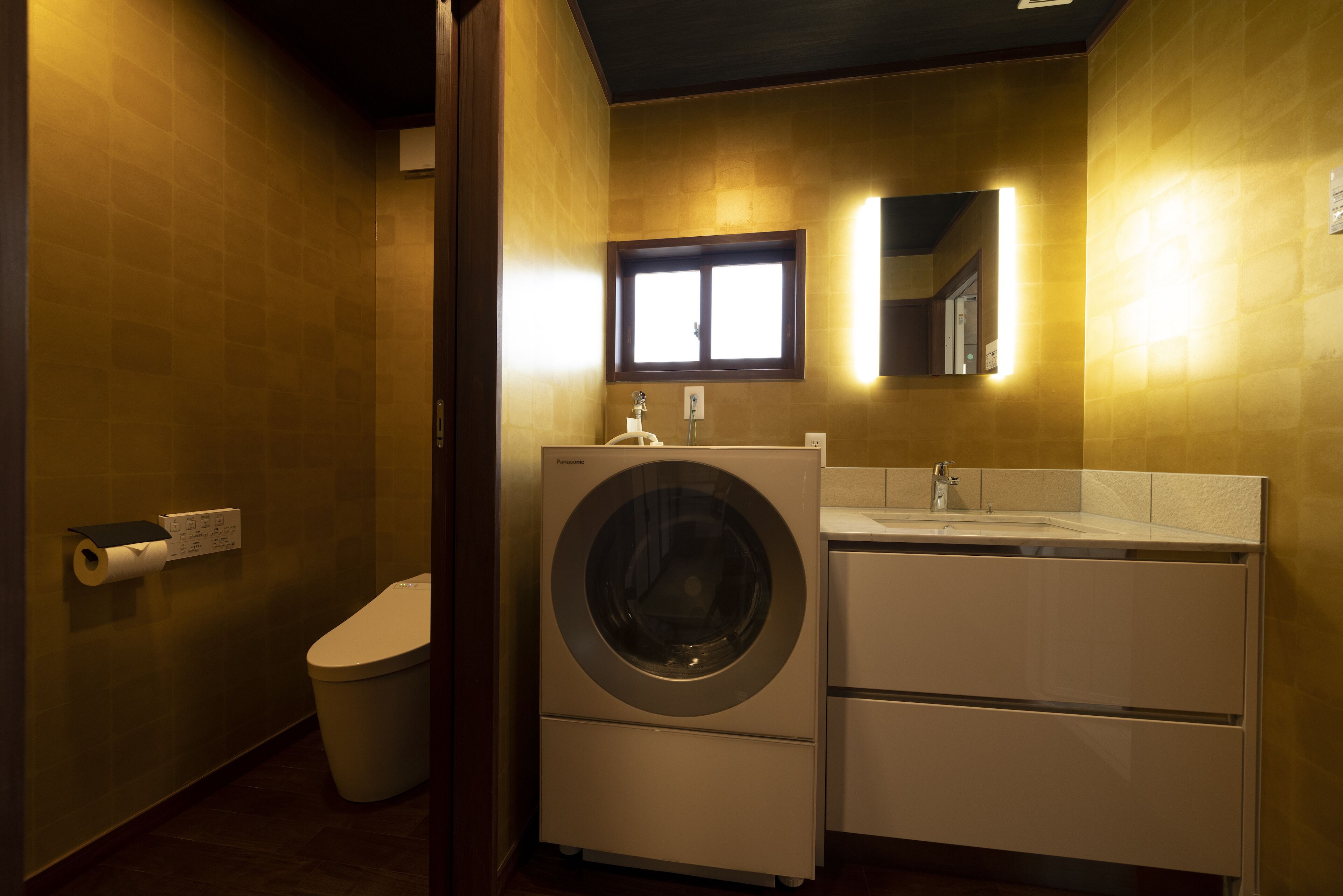 A compact bathroom with a washing machine, toilet, and sink.