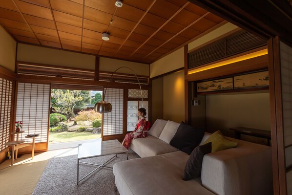 Una habitación tradicional japonesa con suelo de tatami, techo de madera bajo y puertas correderas que dan a un jardín.