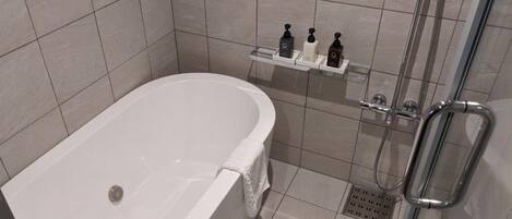 A modern bathroom with a freestanding bathtub, a glass shower enclosure, and a shelf with toiletries.