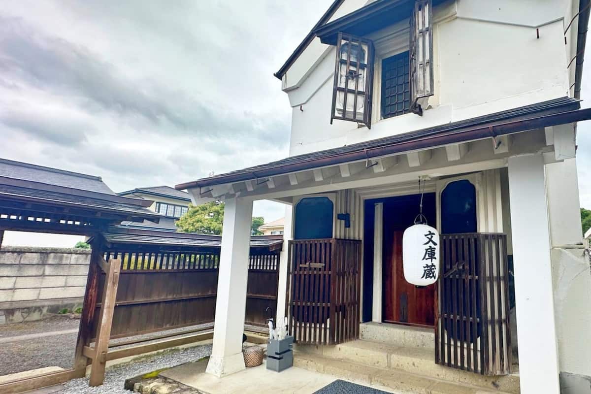 A traditional Japanese house with a wooden gate, a covered porch, and a sign with Japanese characters.