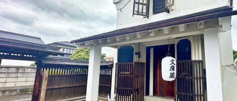 Una casa tradicional japonesa con un portón de madera, un porche cubierto y un letrero con caracteres japoneses.
