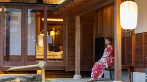 A traditional Japanese building with wooden architecture, a stone pathway, and a person in a kimono sitting on a bench. - Iizukatei (Nakagawa)