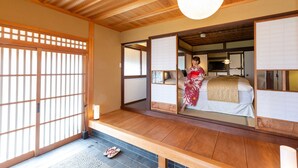 A traditional Japanese room with tatami flooring, a sliding door, and a bed with a red and white patterned kimono. - Iizukatei (Nakagawa)