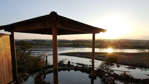 A wooden gazebo with a stone water feature and a view of a river at sunset. - Iizukatei (Nakagawa)