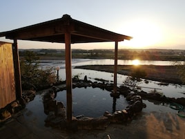 Un pabellón de madera con un elemento acuático de piedra y vista al río al atardecer.