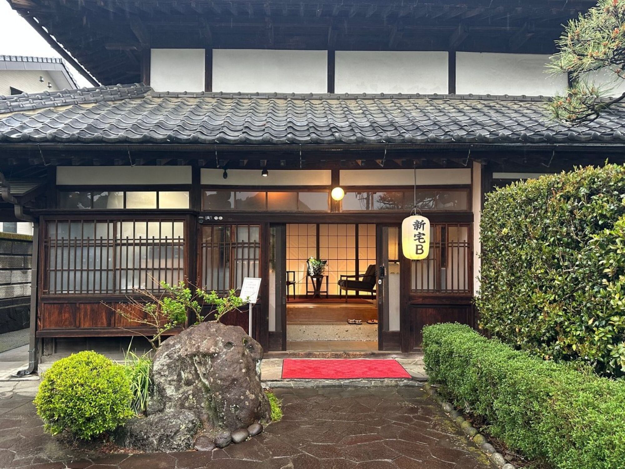 Een traditioneel Japans gebouw met een betegeld dak, houten entree en een rode mat bij de deur.