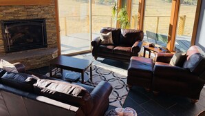 Ein gemütliches Wohnzimmer mit Ledersofas, einem Kamin und großen Fenstern mit Blick auf eine reizvolle Landschaft.