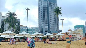A beach with umbrellas and people. Tall buildings are in the background. - Panorama Nha Trang Hotel & Apartments (Nha Trang)