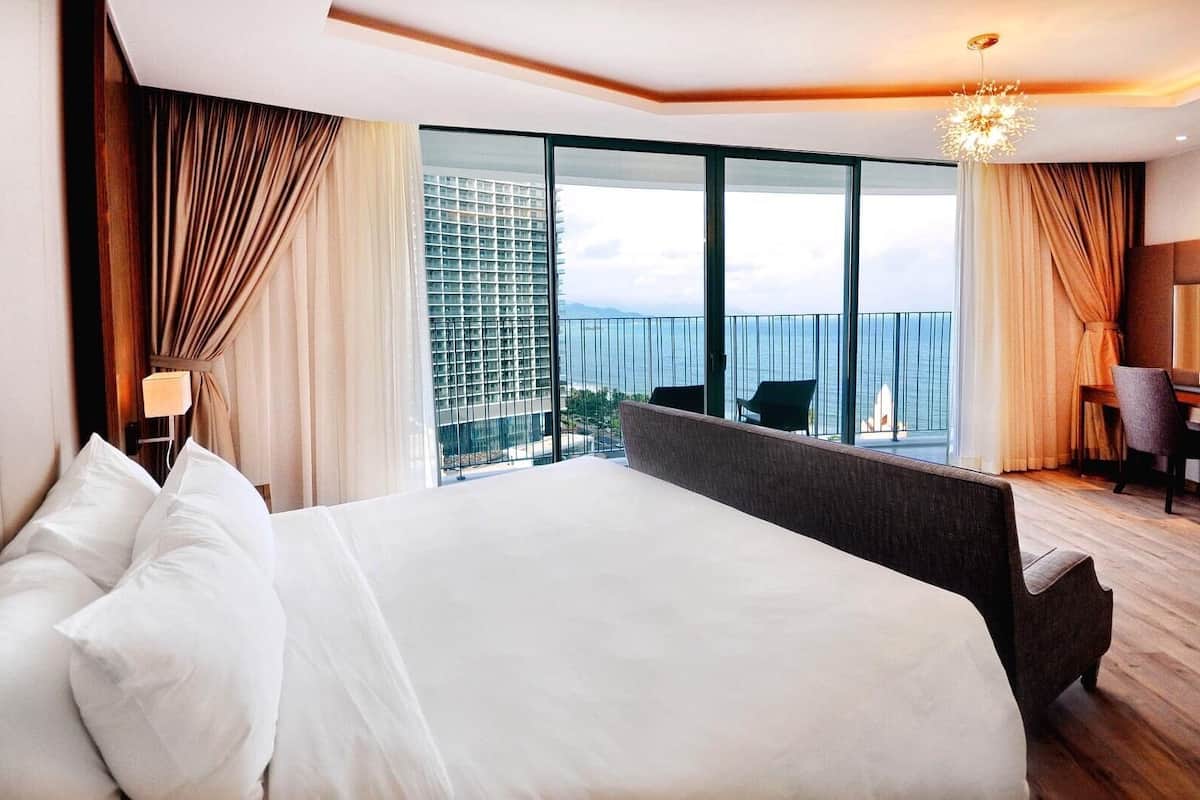 Habitación de hotel con una cama grande, un escritorio y vistas al mar.