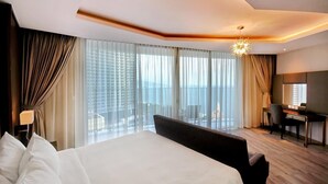 A hotel room with a large bed, a desk, and a view of the city through floor-to-ceiling windows. - Panorama Nha Trang Hotel & Apartments (Nha Trang)