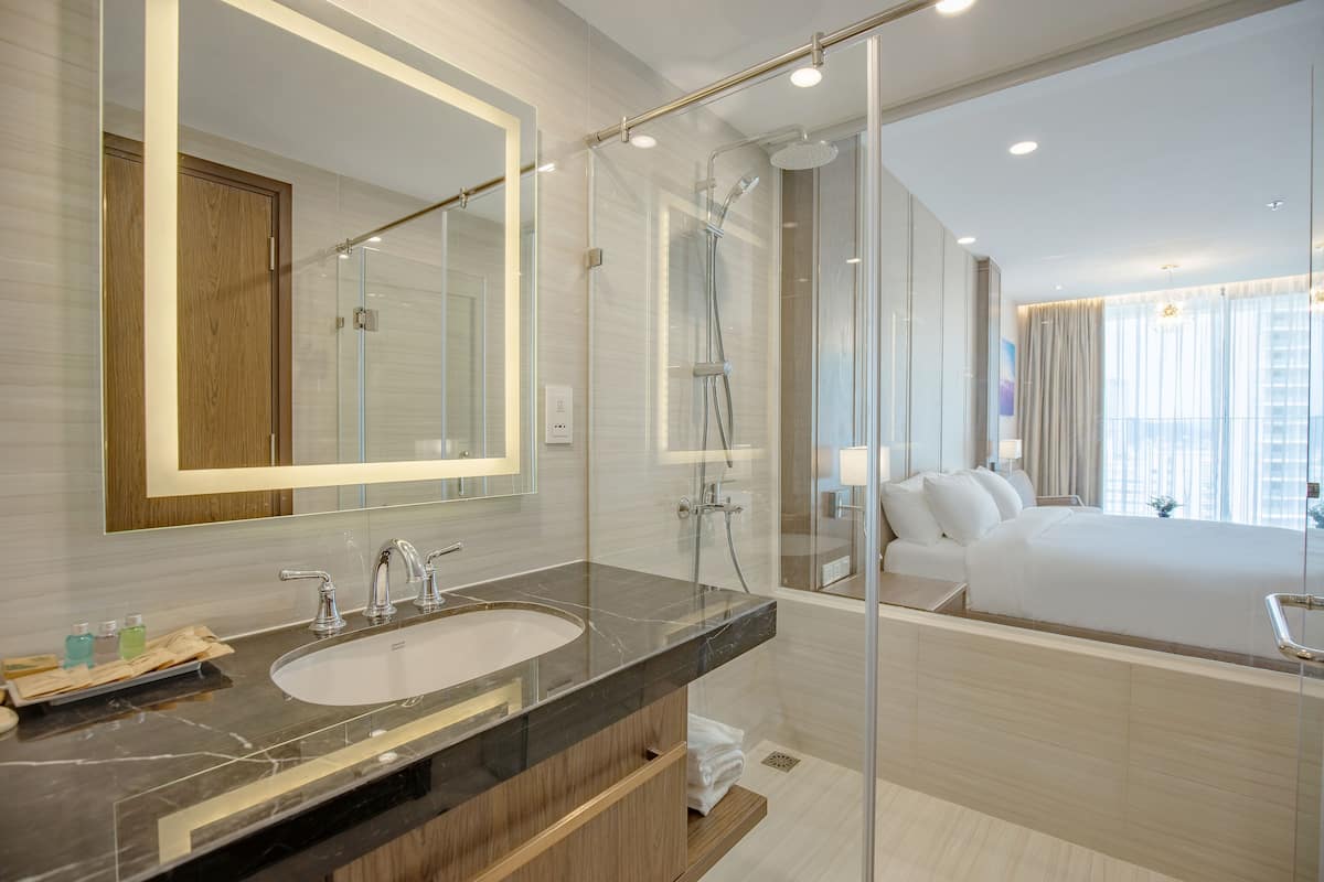 Un baño moderno con cabina de ducha de vidrio, un espejo grande y una habitación separada visible a través del vidrio.
