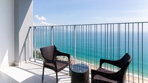 A balcony with two wicker chairs and a small table, overlooking a beach with clear blue water. - Panorama Nha Trang Hotel & Apartments (Nha Trang)