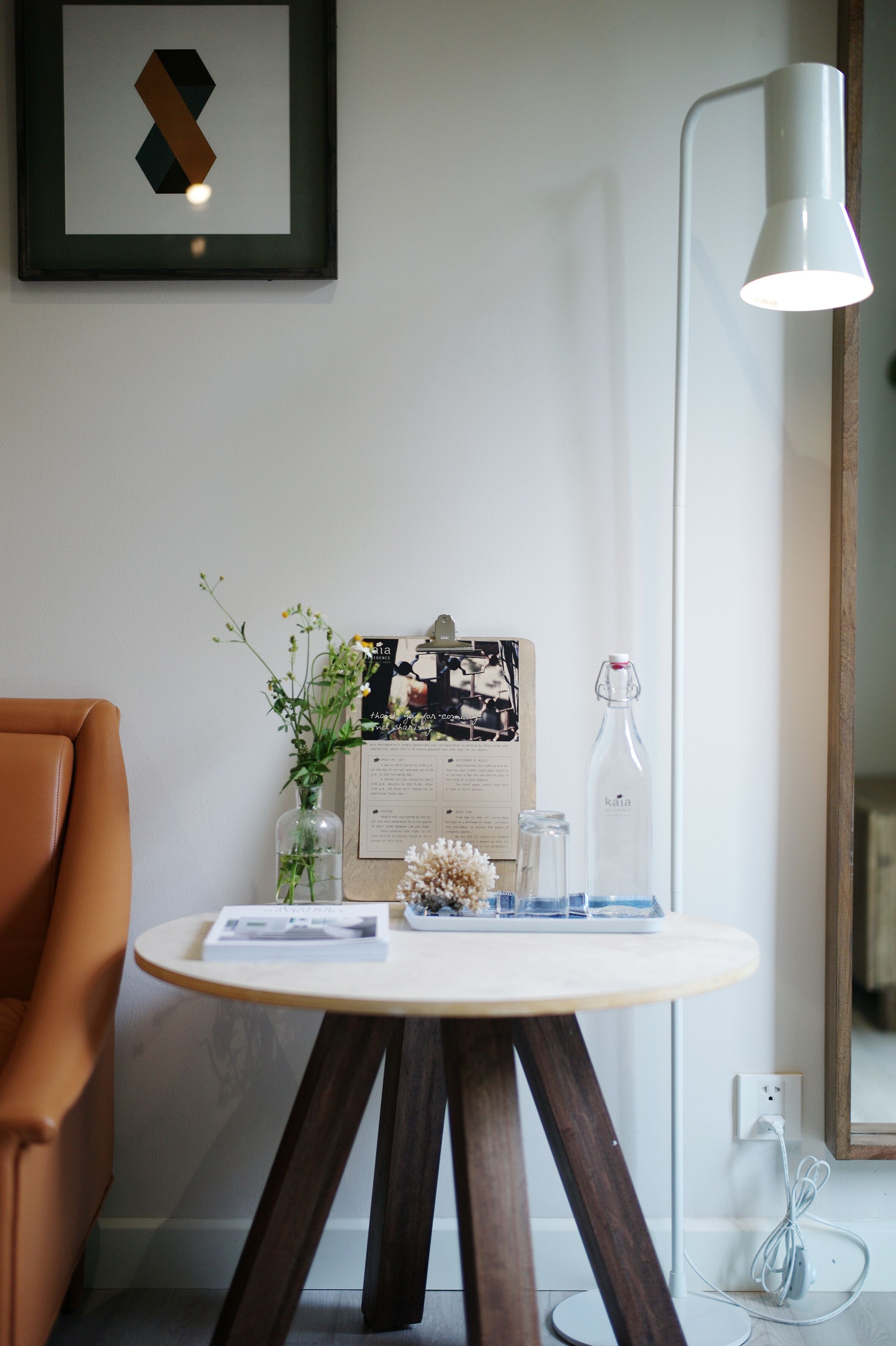Une pièce comprenant une table ronde, une chaise, un tableau encadré, une lampe et un vase avec des fleurs.