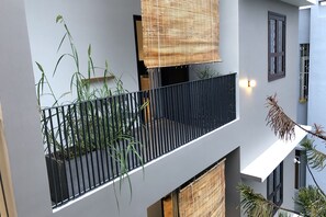 A modern building with a balcony featuring a black railing, potted plants, and a bamboo blind. - Kaia Residence Da Nang Quiet Garden (Da Nang)