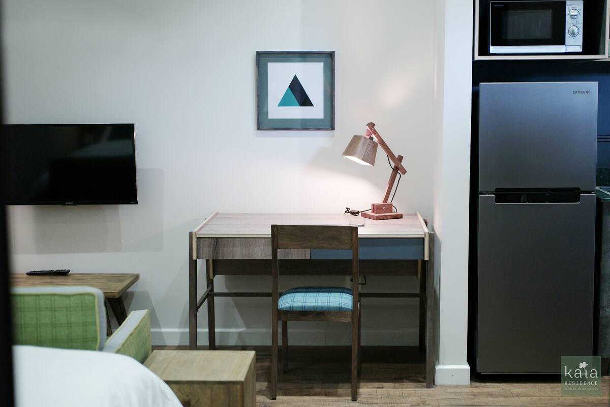 Una habitación pequeña con escritorio, silla, televisor, microondas y refrigerador.