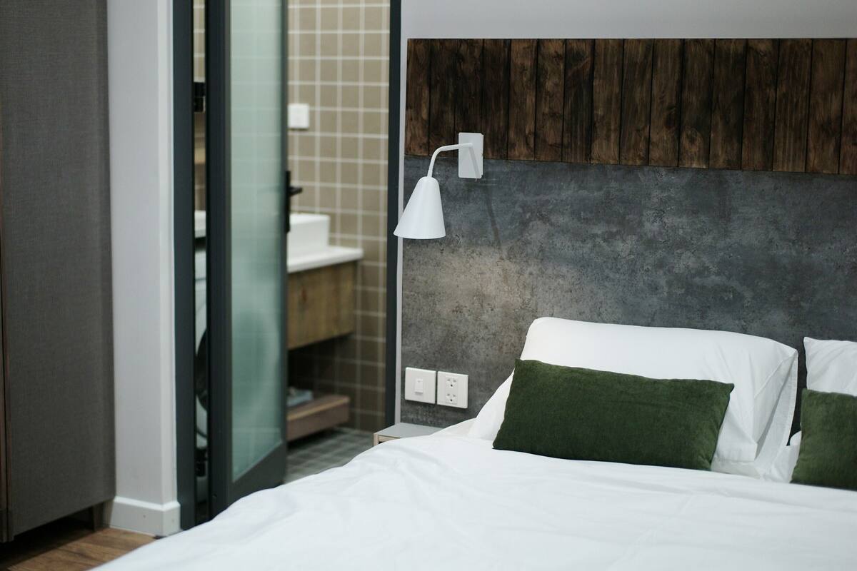 Una habitación de hotel moderna con una cama, una mesita de noche, una lámpara y un cabecero de madera.