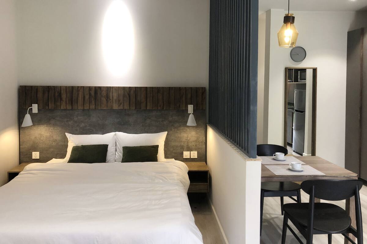 Habitación de hotel moderna con una cama grande, lámparas de noche, un escritorio con sillas y un espejo.