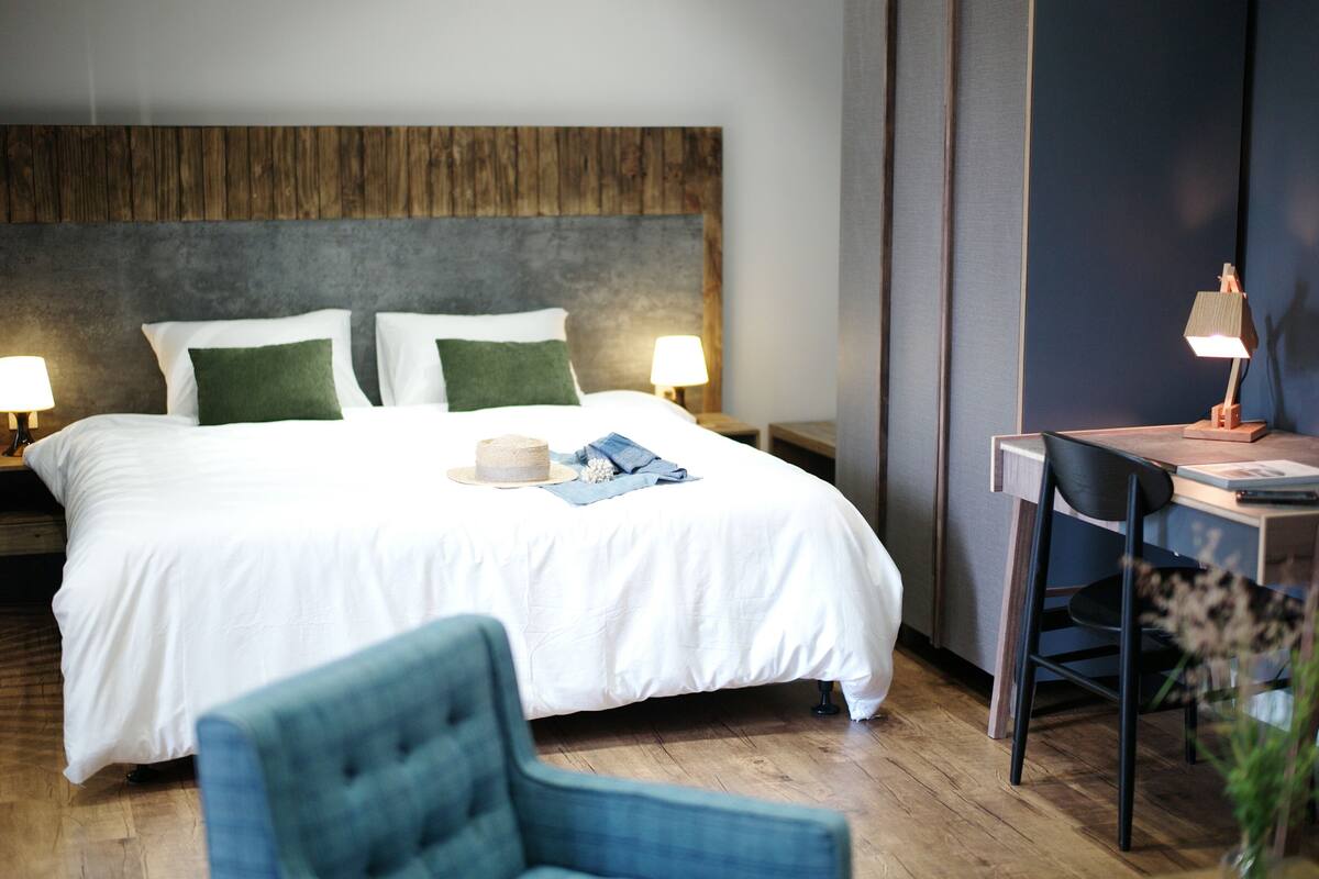 Habitación de hotel con cama, dos lámparas de noche, un escritorio con silla y cabecera de madera.