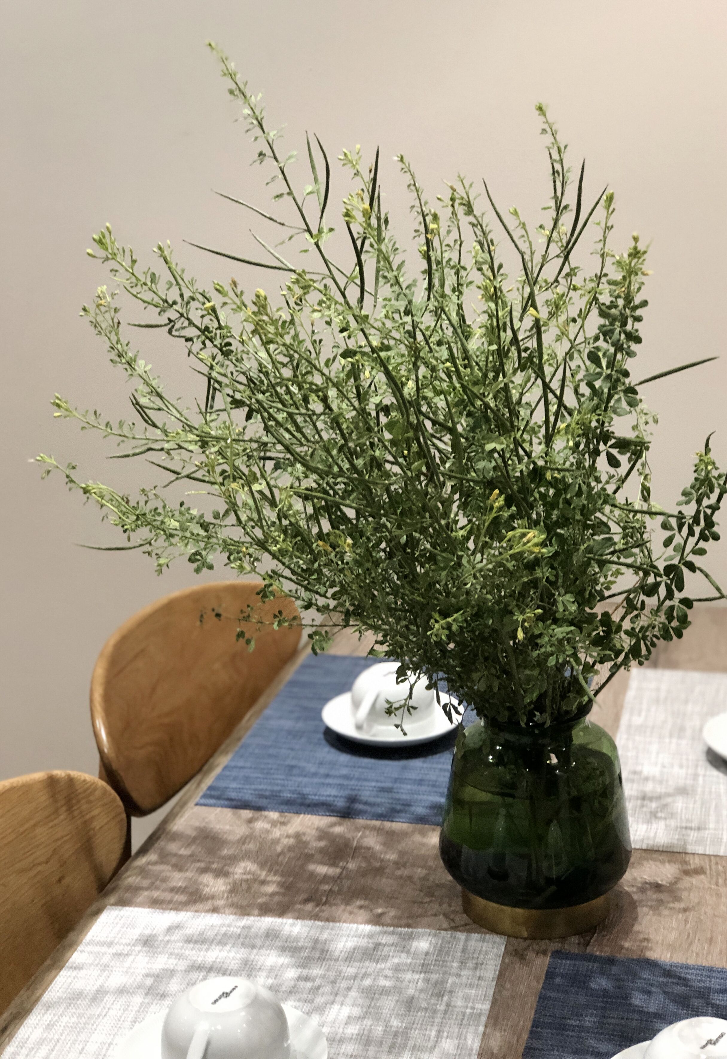 A dining table with a green vase containing a plant, a white teapot, and a blue tablecloth.
