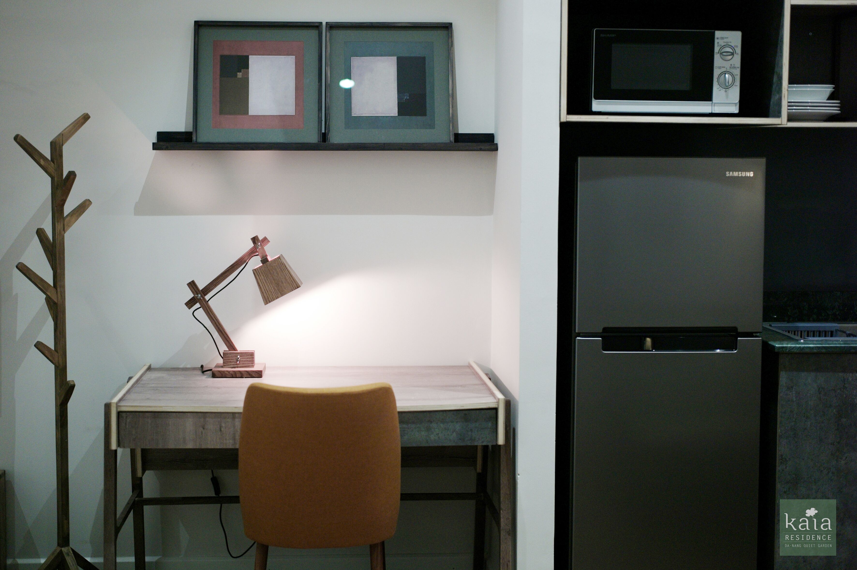 A kitchen with a microwave, refrigerator, and a desk with a lamp.