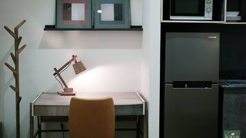 A kitchen with a microwave, refrigerator, and a desk with a lamp.