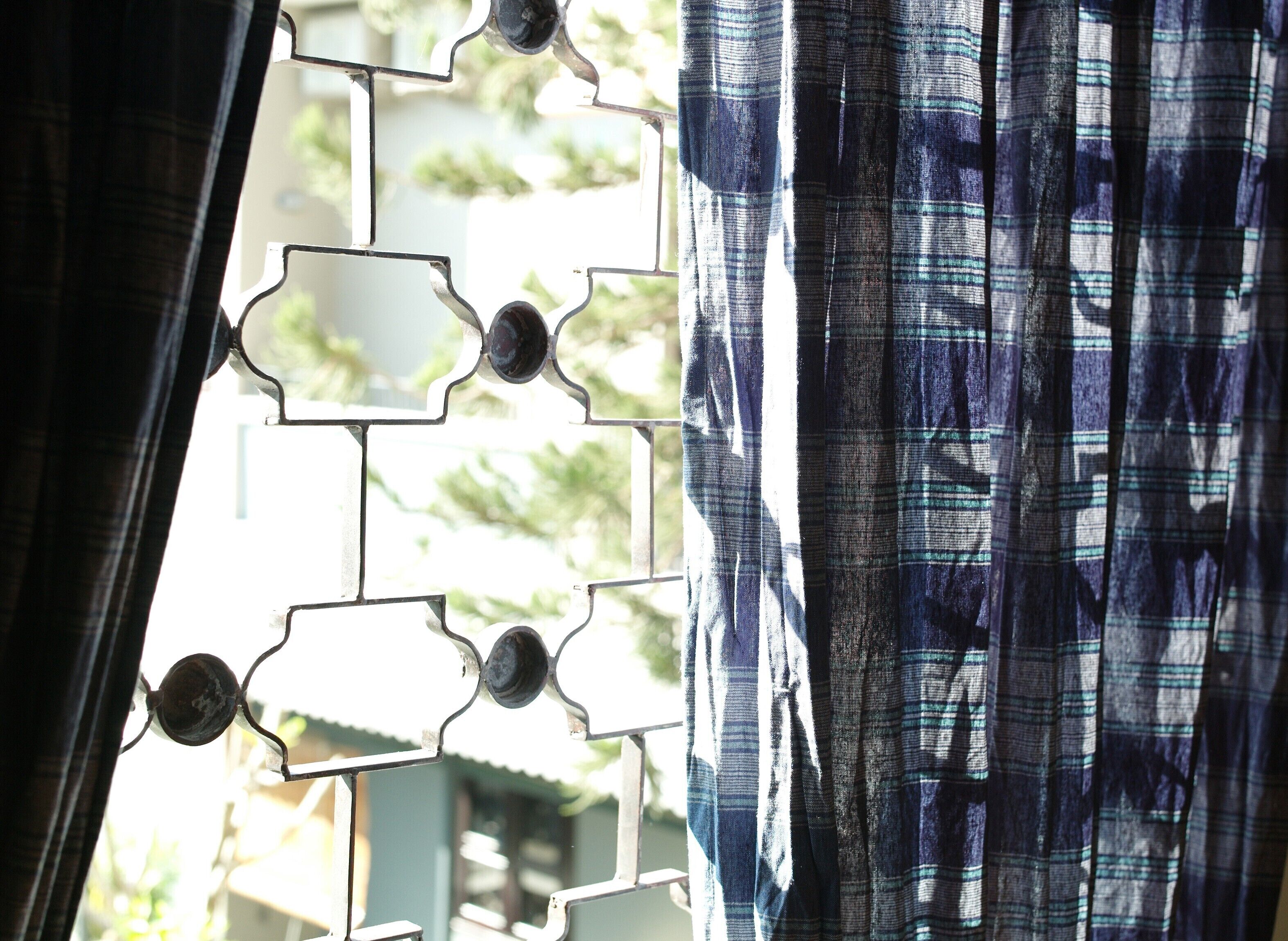 Una ventana con una celosía metálica de diseño y cortinas estampadas.