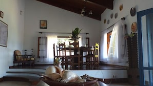 A room with a wooden staircase, a dining area with chairs and a table, and a large window with curtains. - GuestHouse Elephant Ilhabela (Urubu)