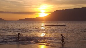 A beach scene with a sunset, calm water, and distant mountains. - GuestHouse Elephant Ilhabela (Urubu)