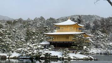 Un edificio tradicional japonés con un tejado simétrico y una entrada central, rodeado de árboles cubiertos de nieve y una masa de agua.