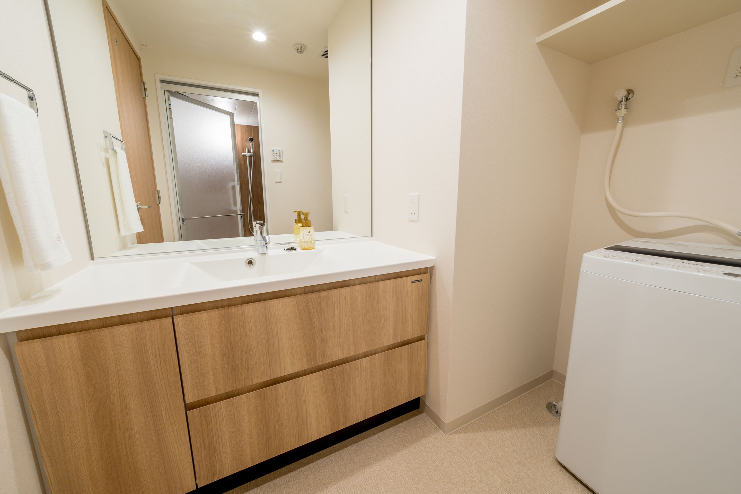 A modern bathroom with a white sink, wooden cabinets, a mirror, and a white washing machine.