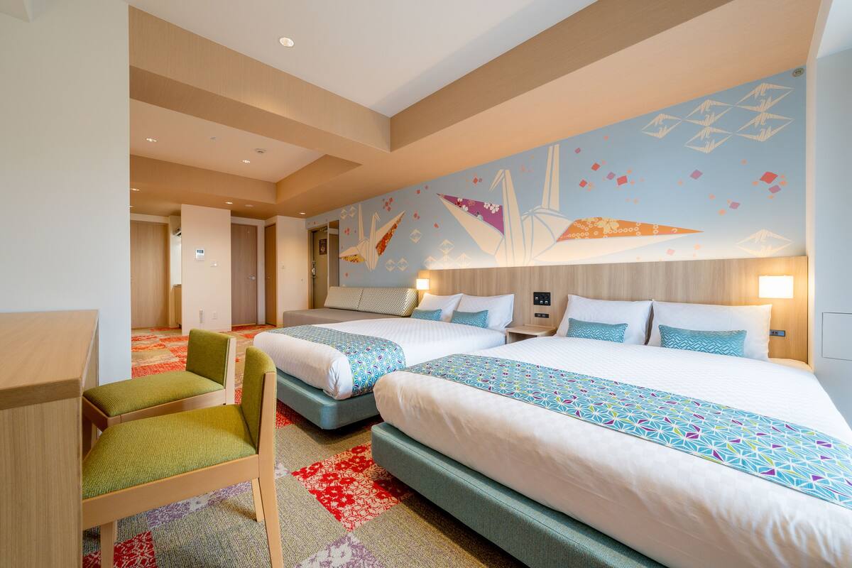 Ett hotellrum med två sängar, ett skrivbord och en stol. Golvet är täckt med matta och en av väggarna har ett geometriskt mönster.