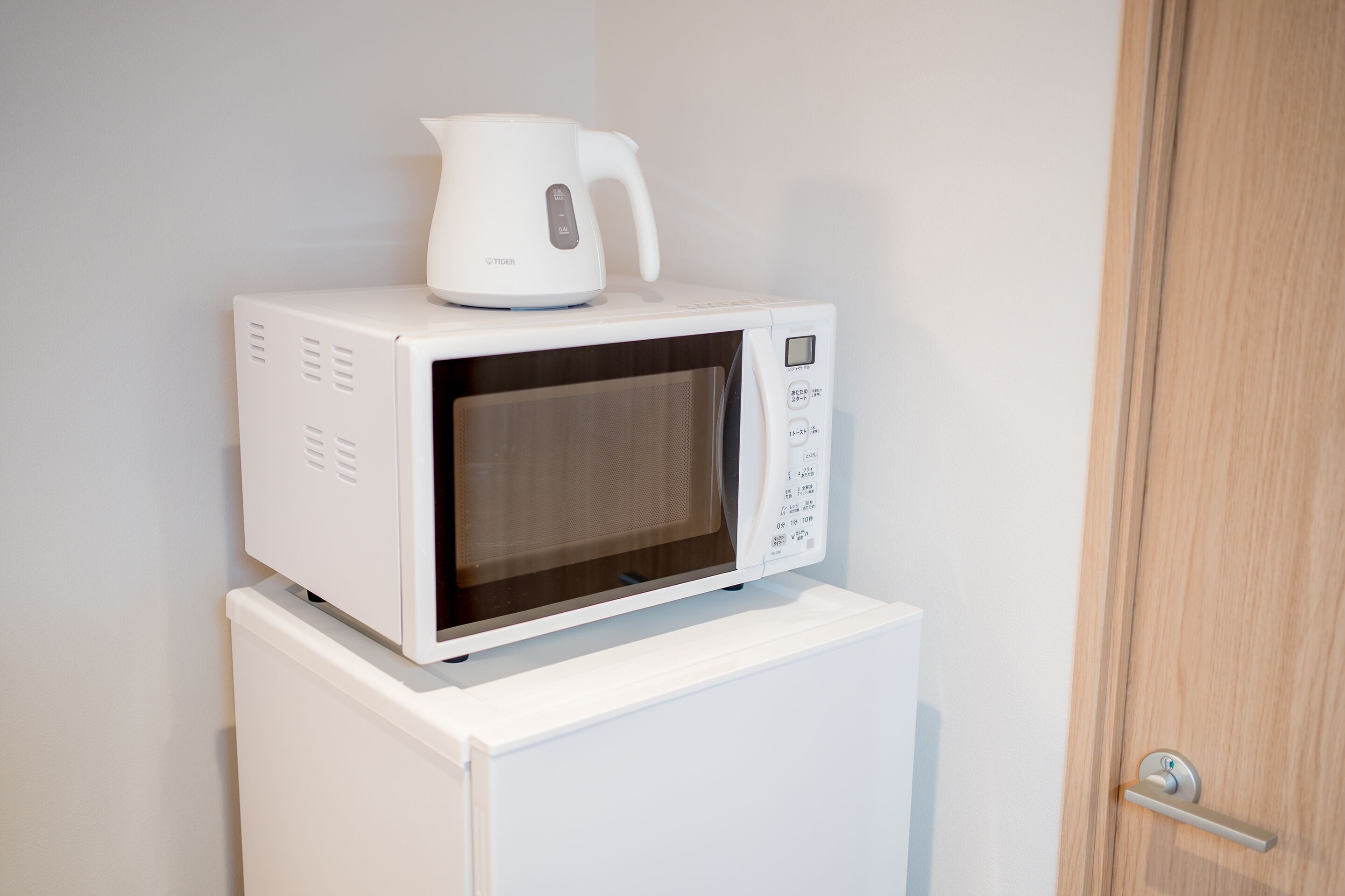 Un horno microondas blanco con una cafetera encima, sobre un mueble blanco.
